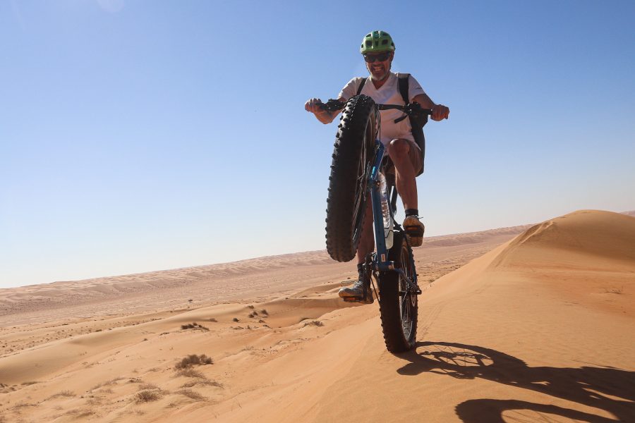 un vététiste en fat bike dans le désert, sur la roue arrière